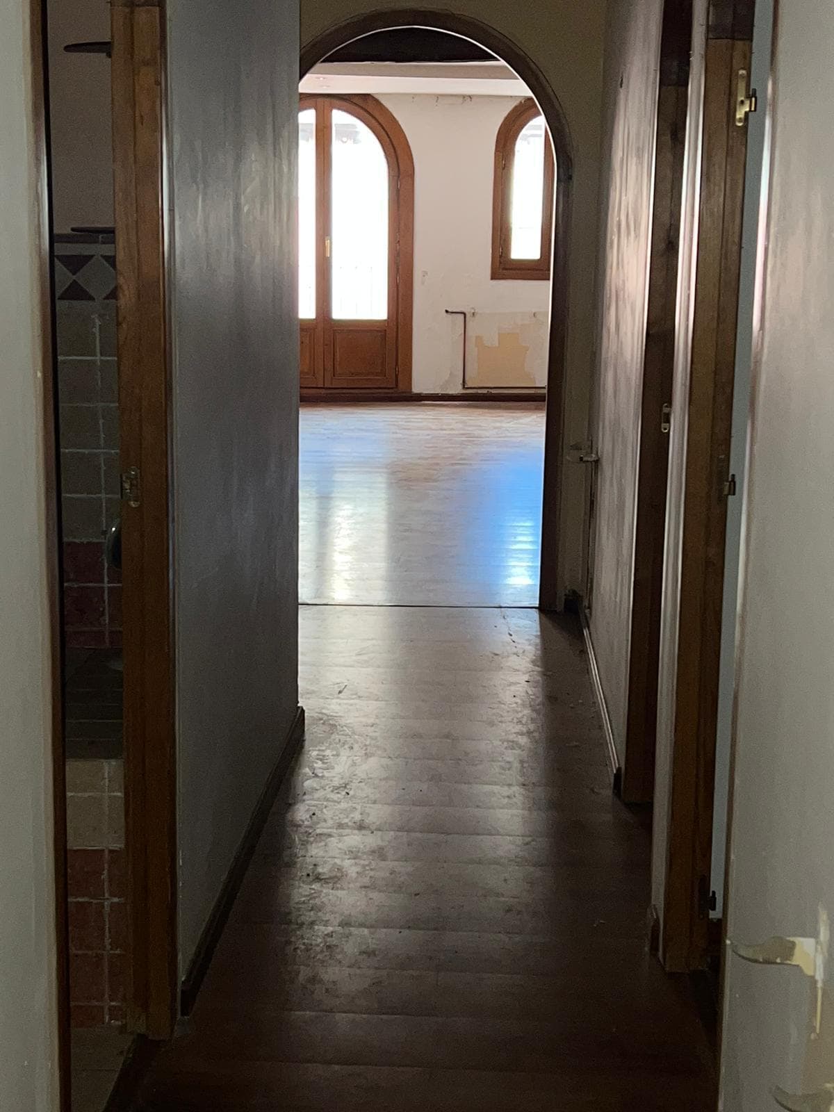 Pasillo con arco antes de la reforma, con suelo de madera deteriorado y carpinterías antiguas